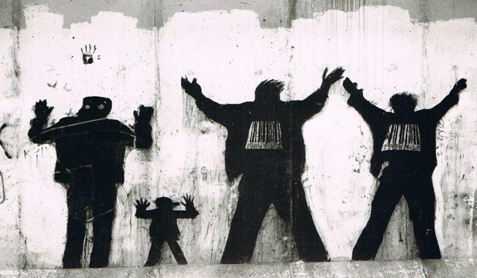 black and white graffiti depicting a group of people in line, hands raised.